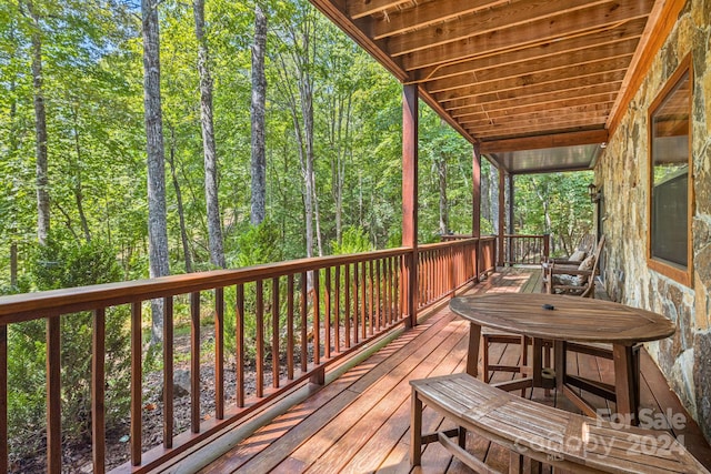 wooden terrace featuring outdoor dining space and a view of trees