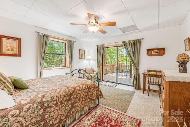 bedroom featuring access to exterior, a paneled ceiling, light colored carpet, and a ceiling fan