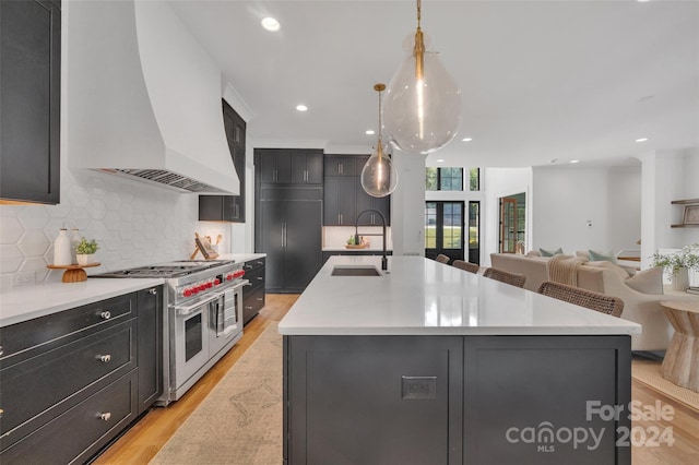 kitchen with decorative light fixtures, custom exhaust hood, a center island with sink, and double oven range