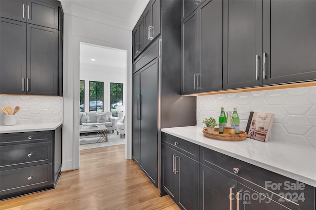 kitchen with light hardwood / wood-style floors, ornamental molding, light stone countertops, and tasteful backsplash