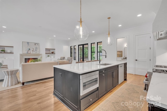 kitchen with pendant lighting, sink, a center island with sink, appliances with stainless steel finishes, and light wood-type flooring