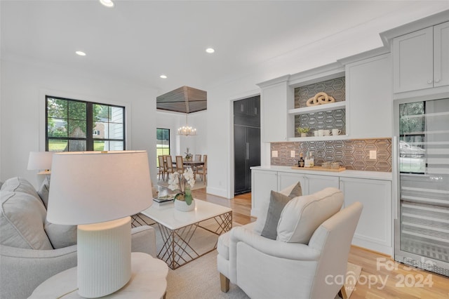 living room featuring an inviting chandelier, indoor bar, light hardwood / wood-style floors, and beverage cooler