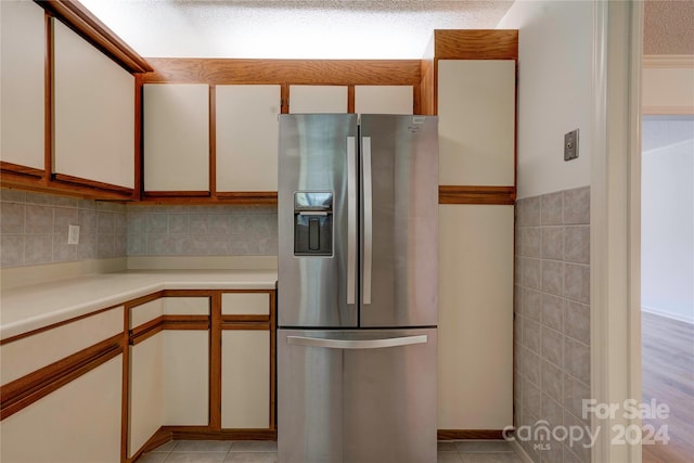 kitchen with a textured ceiling, stainless steel refrigerator with ice dispenser, light tile patterned floors, tile walls, and white cabinets