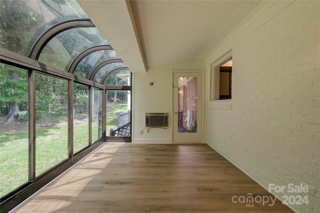 unfurnished sunroom featuring lofted ceiling, a healthy amount of sunlight, and a wall unit AC