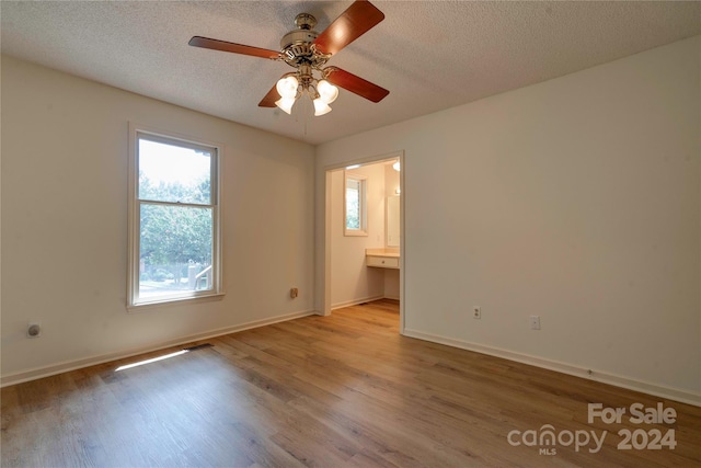 unfurnished bedroom with a textured ceiling, light hardwood / wood-style flooring, ceiling fan, and ensuite bath