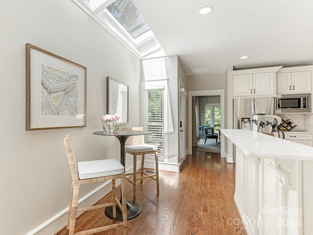 kitchen with appliances with stainless steel finishes, white cabinets, vaulted ceiling with skylight, and wood-type flooring