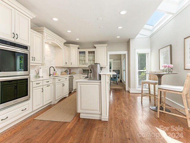 kitchen featuring hardwood / wood-style floors, lofted ceiling with skylight, white cabinetry, backsplash, and a kitchen island