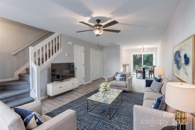 living area featuring visible vents, a ceiling fan, wood finished floors, baseboards, and stairs