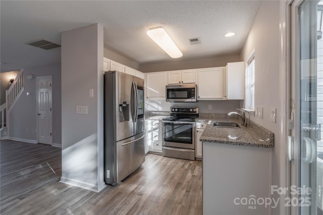 kitchen featuring visible vents, white cabinets, stone countertops, stainless steel appliances, and a sink