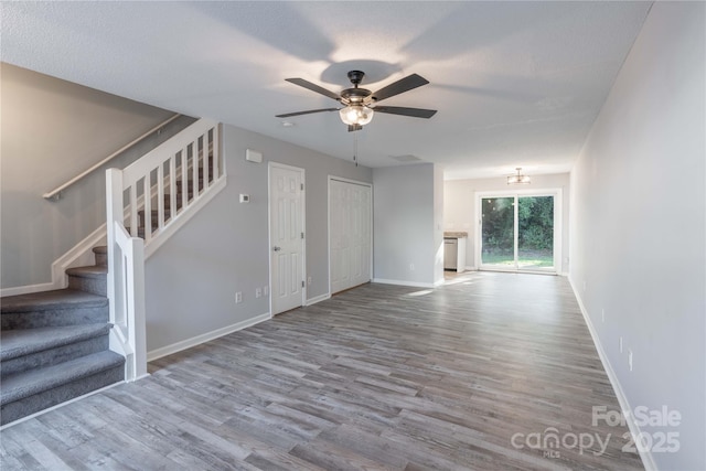 unfurnished living room featuring a ceiling fan, stairway, wood finished floors, and baseboards