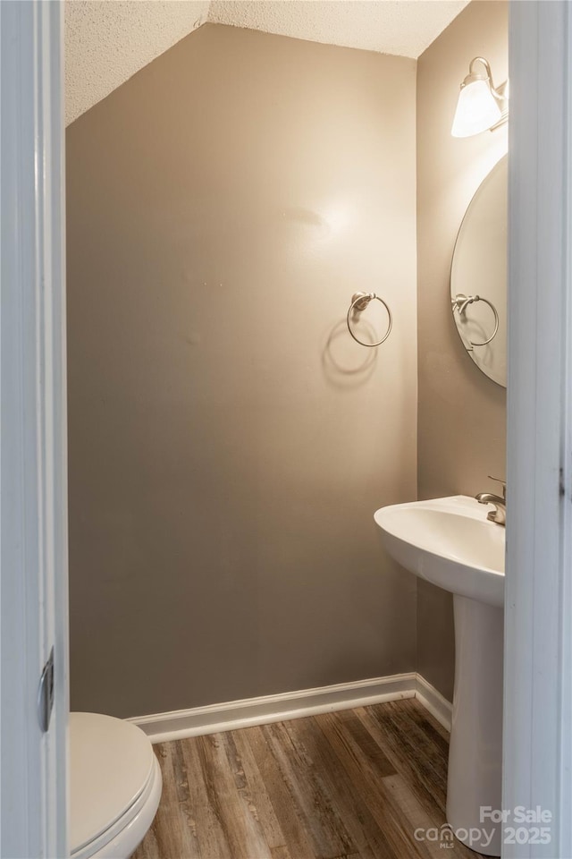 half bathroom featuring toilet, a sink, wood finished floors, baseboards, and vaulted ceiling