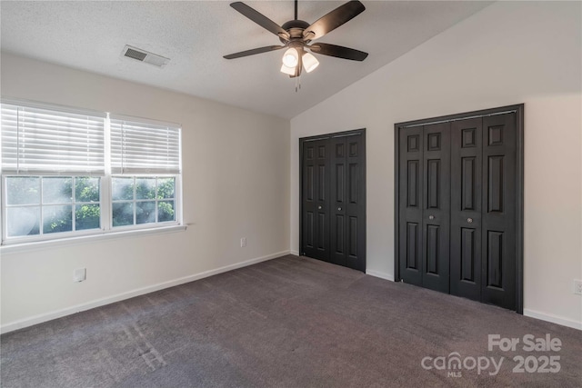 unfurnished bedroom with dark colored carpet, visible vents, multiple closets, and lofted ceiling