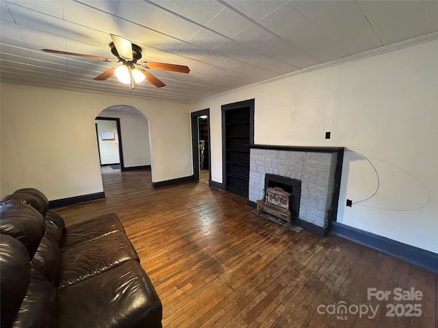 unfurnished living room with ceiling fan, crown molding, dark hardwood / wood-style floors, and a stone fireplace