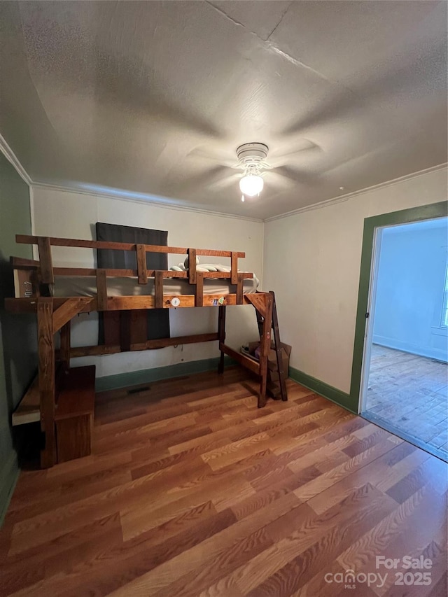 bedroom featuring ceiling fan, a textured ceiling, ornamental molding, and hardwood / wood-style floors