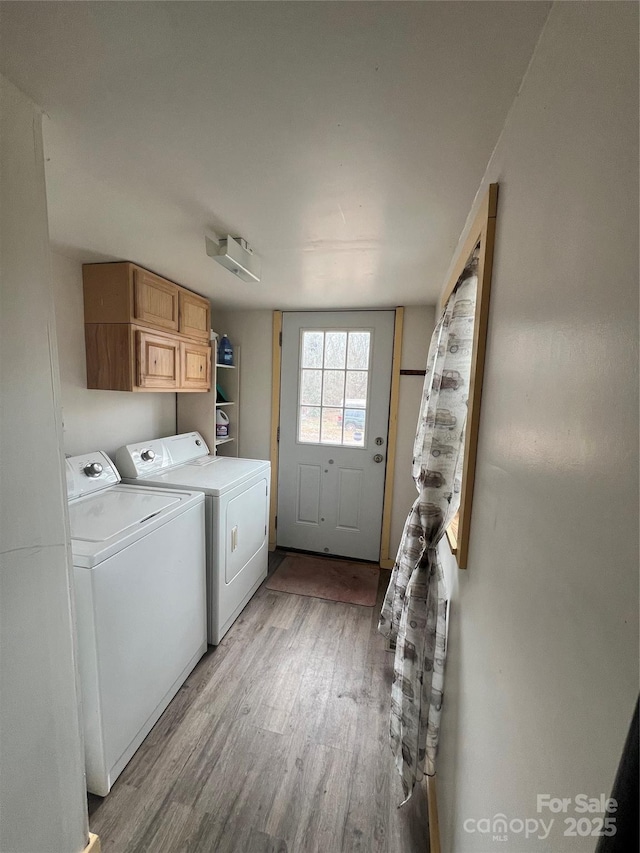 laundry area with light wood-type flooring, washing machine and dryer, and cabinets