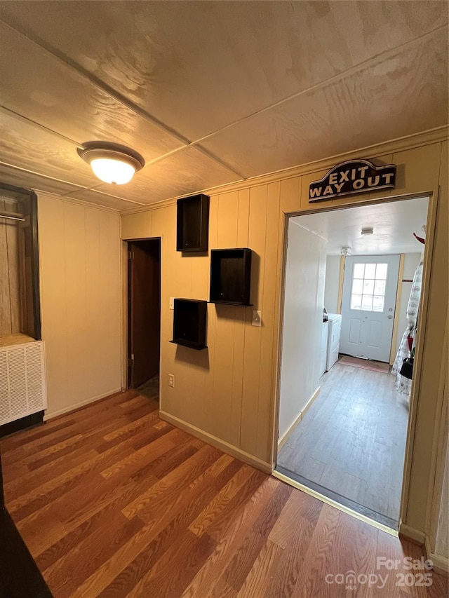 corridor with hardwood / wood-style floors, washing machine and clothes dryer, wooden walls, and radiator heating unit