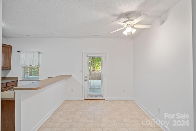 interior space featuring a textured ceiling, kitchen peninsula, and ceiling fan