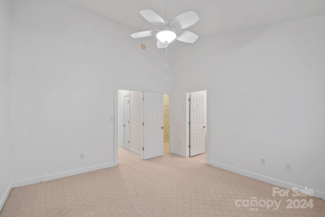 carpeted empty room with a towering ceiling and ceiling fan