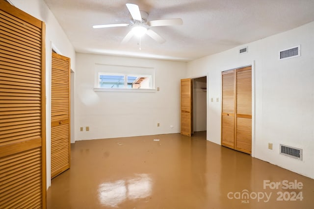 unfurnished bedroom featuring a textured ceiling, ceiling fan, two closets, and concrete floors