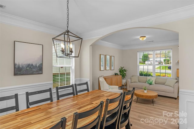 dining space with arched walkways, light wood-style flooring, visible vents, ornamental molding, and an inviting chandelier