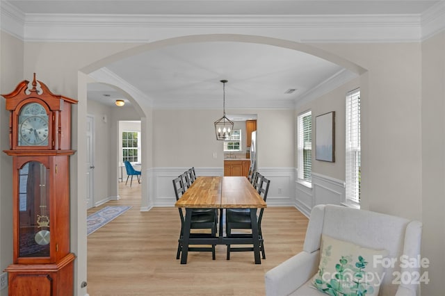 dining room with arched walkways, wainscoting, crown molding, and light wood finished floors