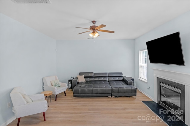 living area with light wood finished floors, a fireplace with flush hearth, baseboards, and a ceiling fan