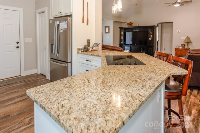 kitchen featuring stainless steel fridge, white cabinetry, hardwood / wood-style floors, and light stone countertops