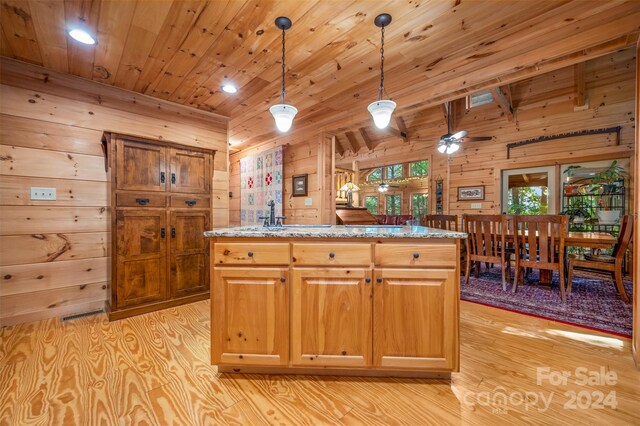 kitchen featuring light wood-type flooring, hanging light fixtures, light stone counters, and wooden walls