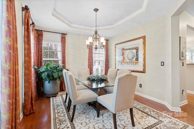 dining space with a chandelier, wood-type flooring, a tray ceiling, and ornamental molding