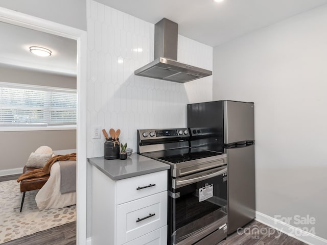 kitchen with wall chimney exhaust hood, white cabinets, appliances with stainless steel finishes, and dark hardwood / wood-style floors