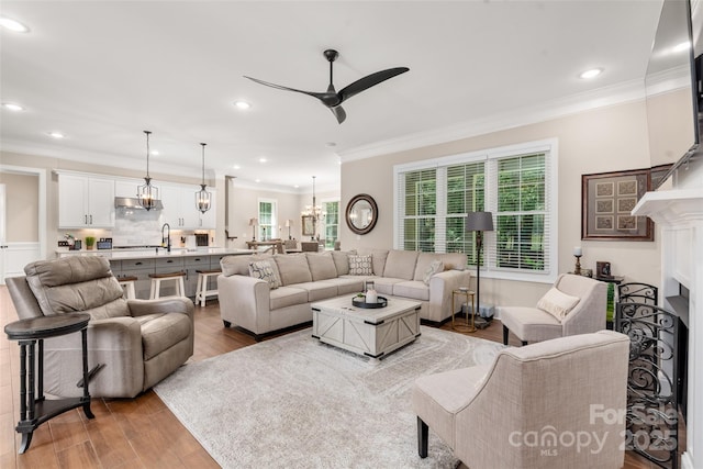 living room featuring ceiling fan with notable chandelier, wood finished floors, a fireplace, and ornamental molding