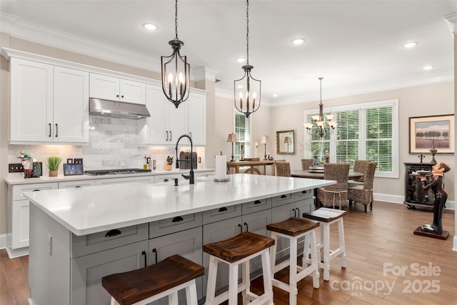 kitchen with ornamental molding, under cabinet range hood, stainless steel gas stovetop, light wood finished floors, and light countertops