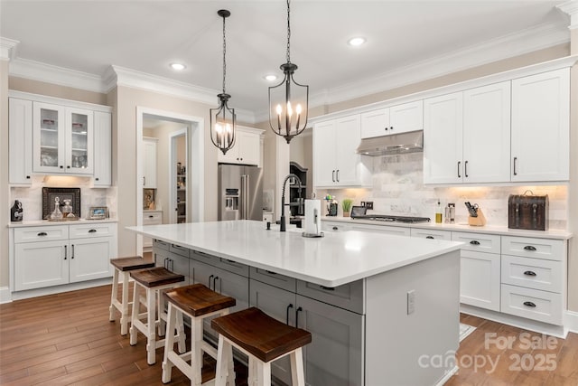 kitchen featuring white cabinetry, backsplash, a center island with sink, stainless steel appliances, and a kitchen bar