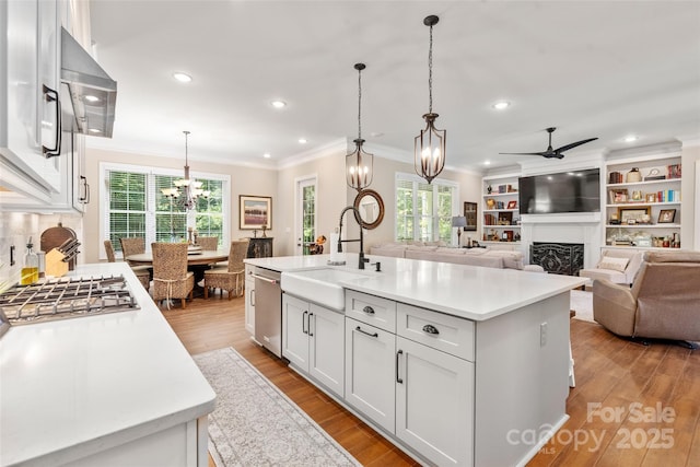 kitchen with sink, white cabinetry, hanging light fixtures, stainless steel dishwasher, and a kitchen island with sink