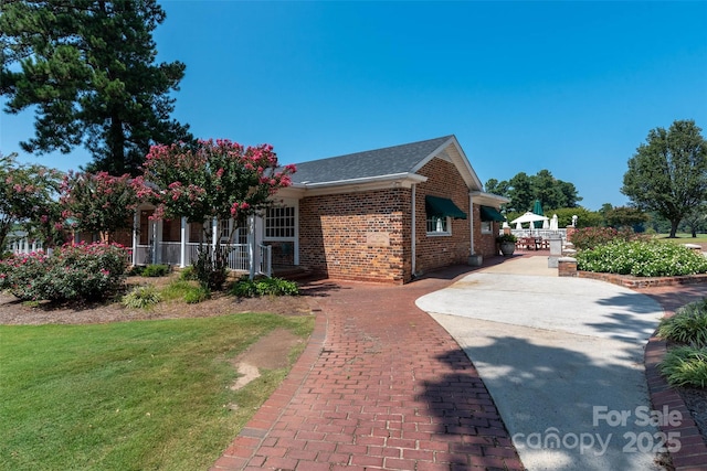 view of front of home with a front yard, decorative driveway, covered porch, and brick siding