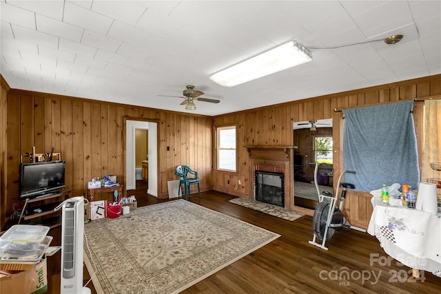 living room with dark wood-type flooring, wood walls, ceiling fan, and a brick fireplace