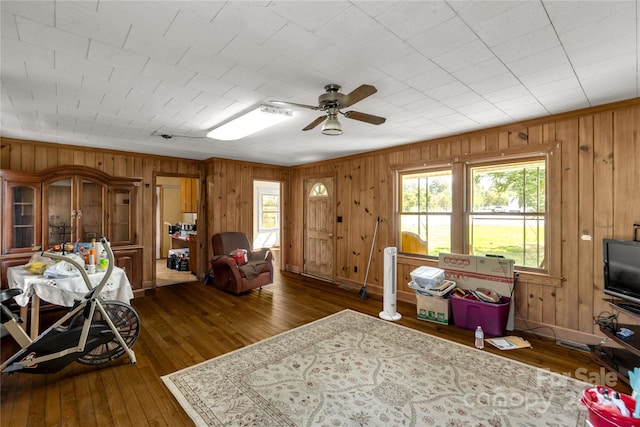 living room with dark wood-type flooring, ceiling fan, and wooden walls