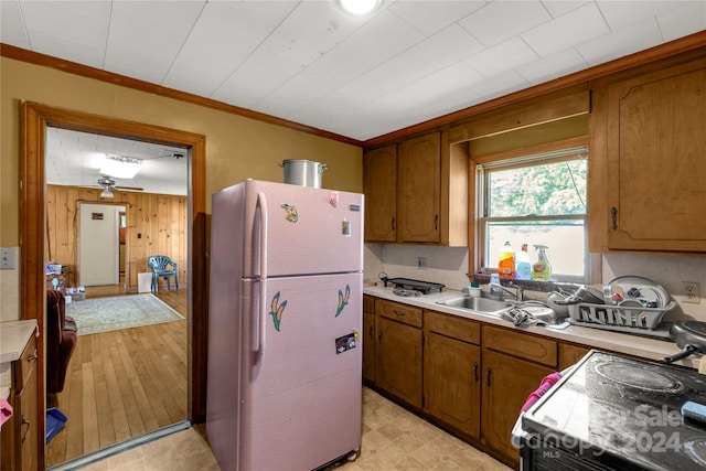 kitchen with light wood-type flooring, wooden walls, white fridge, ornamental molding, and electric range