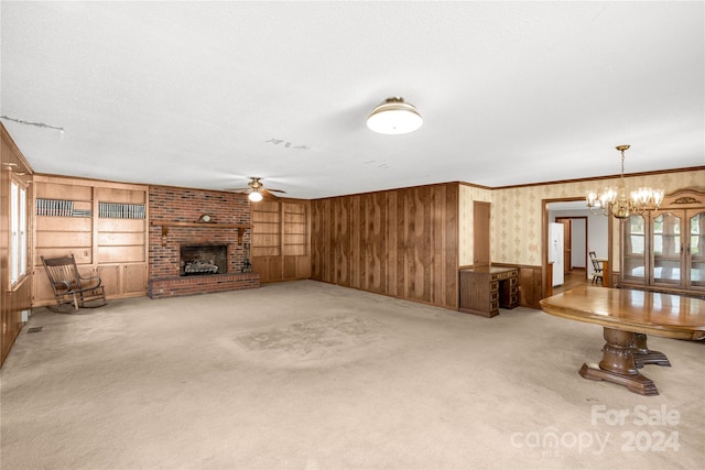 unfurnished living room featuring brick wall, ceiling fan with notable chandelier, a fireplace, carpet, and built in shelves