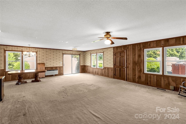 unfurnished living room with a textured ceiling, carpet flooring, ceiling fan, and wooden walls