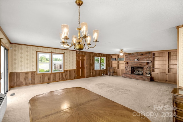 unfurnished living room with a wealth of natural light, ceiling fan with notable chandelier, carpet floors, and wooden walls