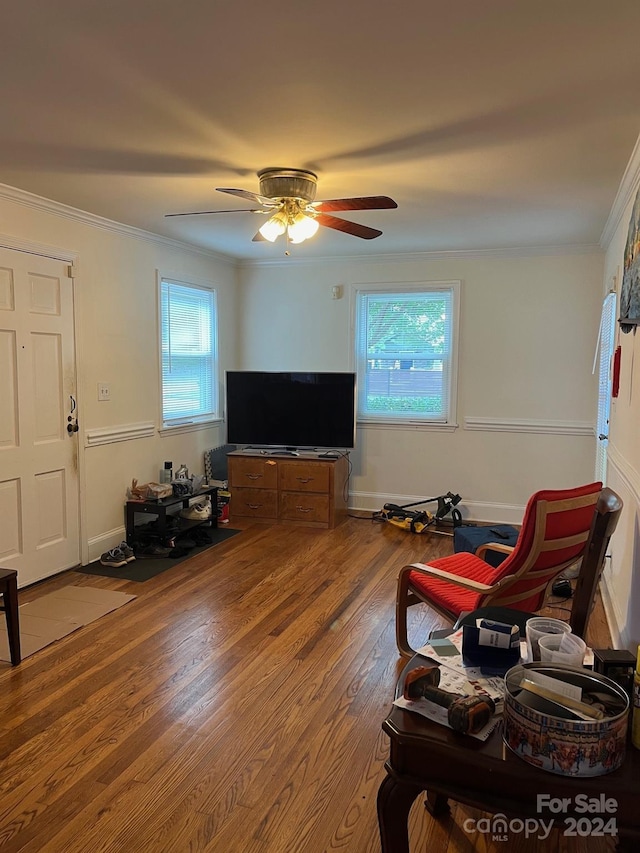 living area with ornamental molding, ceiling fan, wood finished floors, and a healthy amount of sunlight