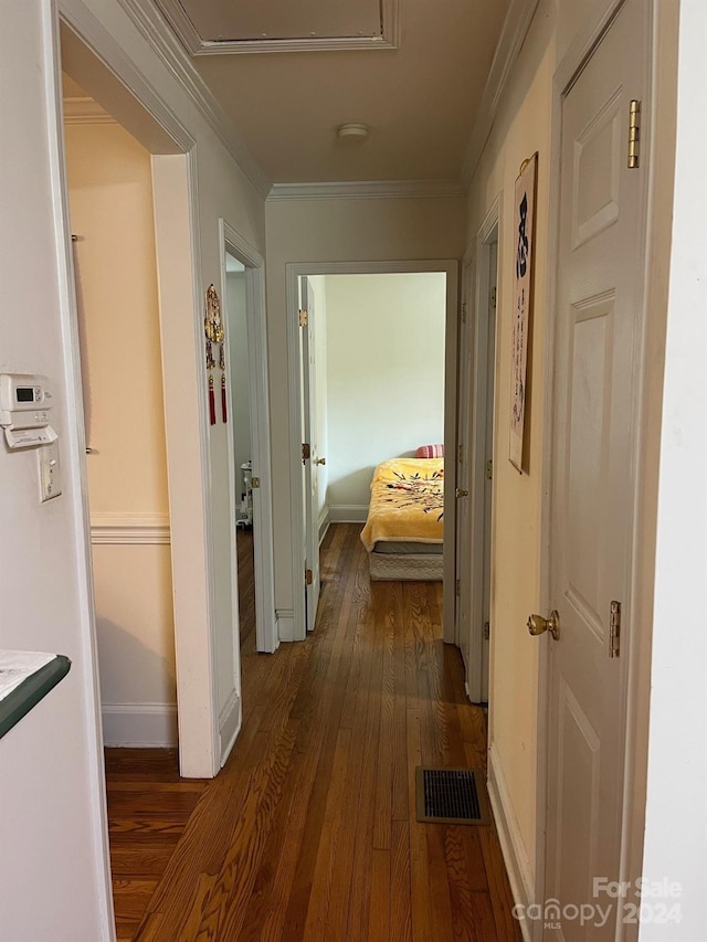 hall featuring dark wood-type flooring, visible vents, crown molding, and baseboards