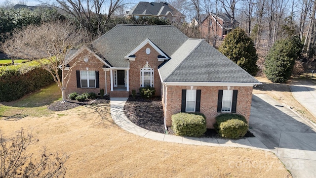 traditional home with brick siding, concrete driveway, a shingled roof, and a front lawn