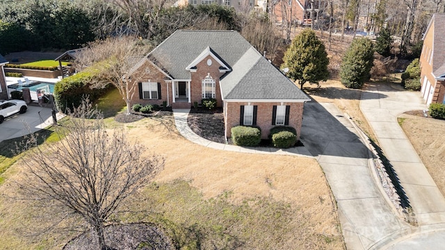 view of front of home with concrete driveway, brick siding, and roof with shingles