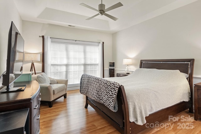 bedroom featuring a tray ceiling, wood finished floors, visible vents, and ceiling fan