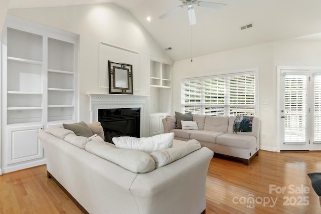 living area featuring visible vents, light wood-style flooring, ceiling fan, and a glass covered fireplace