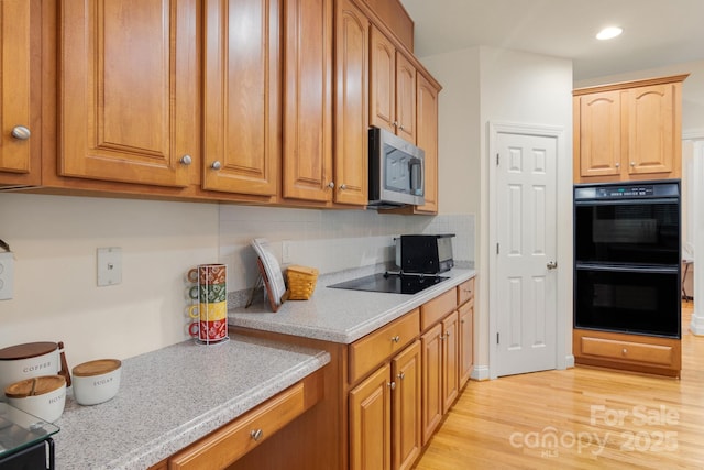 kitchen with brown cabinets, black appliances, recessed lighting, light wood finished floors, and decorative backsplash