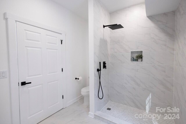 bathroom with toilet, a tile shower, and tile patterned floors