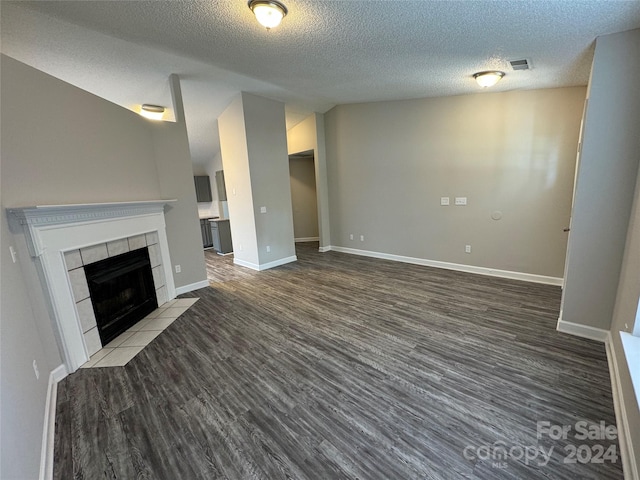 unfurnished living room featuring wood-type flooring, a textured ceiling, and a tile fireplace